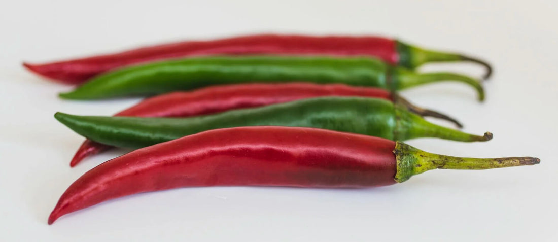  Red and green cayenne peppers lined up on a white background, showcasing the vibrant colors and natural health benefits of this spicy superfood.